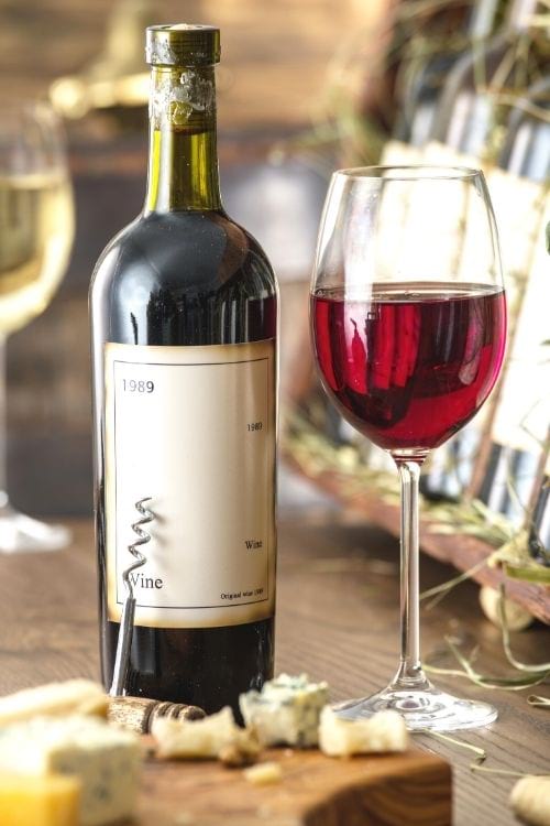 Une bouteille de vin et un verre à pied sur une table en bois avec du fromage.