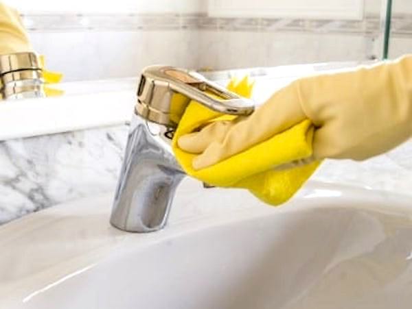 Une main dans un gant en de nettoyage qui essuie un robinet de salle de bain.