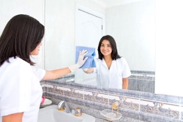 Une jeune femme qui nettoie un miroir avec de l'eau oxygénée.