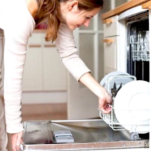 Une femme qui range des assiettes dans un lave-vaisselle propre.