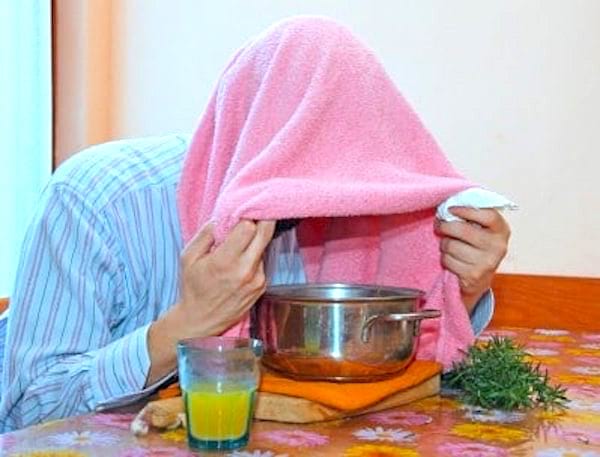 Un homme enrhumé qui se soigne en faisant une inhalation avec une serviette sur sa tête.