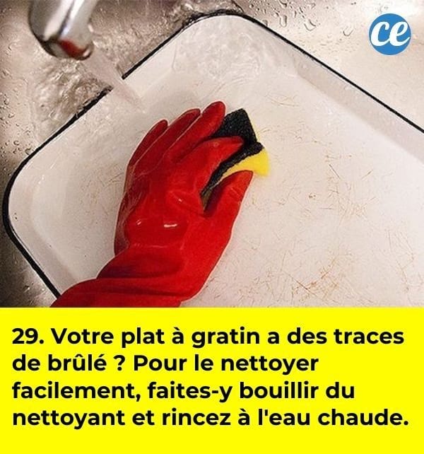 Des mains avec un gant de nettoyage rouge qui passent une éponge sur un plat en fonte émaillée, dans un évier.