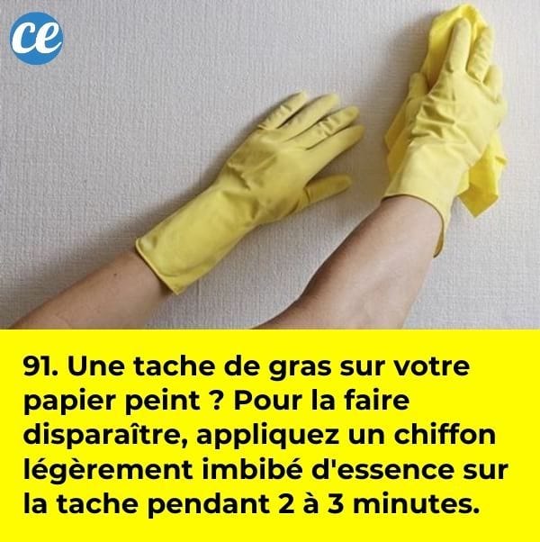 Des mains dans des gants de nettoyage en latex jaune qui nettoie une tache de gras sur du papier peint de couleur claire.