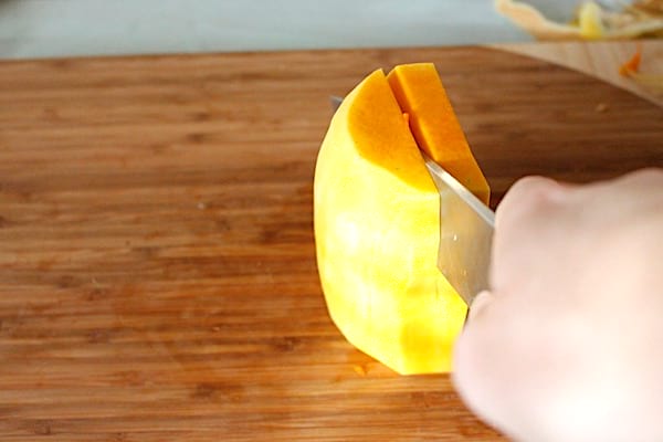 Une main avec un couteau qui coupe la courge butternut en hauteur