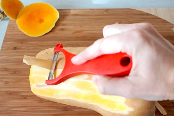 Une main qui épluche la courge butternut avec un économe