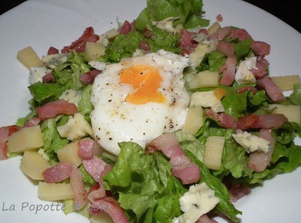 un oeuf poché cuit au micro ondes sur une salade verte avec des lardons