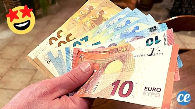 Des billets de 50 euros, 20 euros et 10 euros dans la main au dessus d'une table en bois