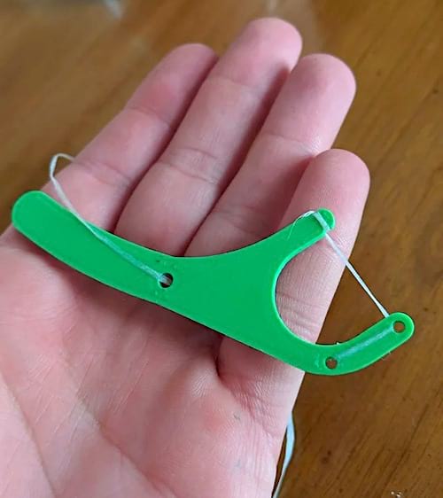 Un porte fil dentaire vert sur une main pour enlever les restes de nourriture entre les dents