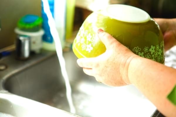 Des mains qui finissent la vaisselle au dessus de l'évier avec un bol propre