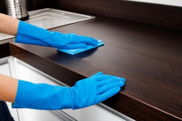 des mains dans des gants bleus qui essuient le plan de travail de la cuisine