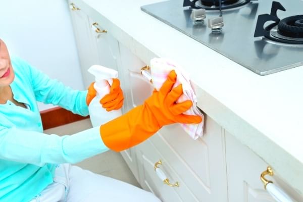 Une femme qui nettoie les portes des placards bas de la cuisine avec un spray nettoyant
