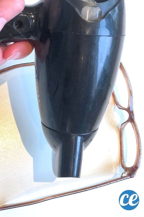 Une personne chauffe la monture en plastique d'une paire de lunettes rouge avec un sèche cheveux