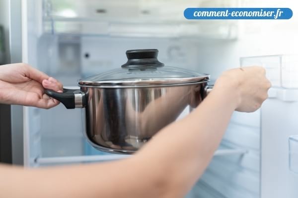 Une femme qui met une casserole chaude dans le réfrigérateur.
