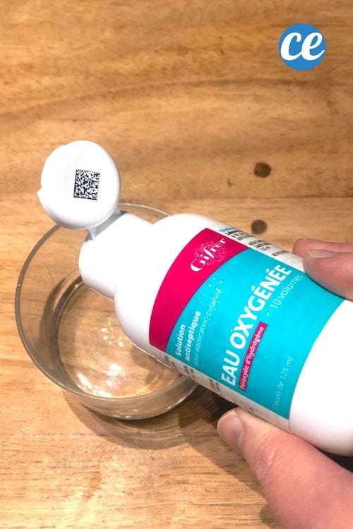 de l'eau oxygénée est versée dans un récipient transparent posé sur une table en bois