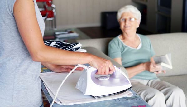 Une femme qui fait le repassage pour une personne âgée qui est assise