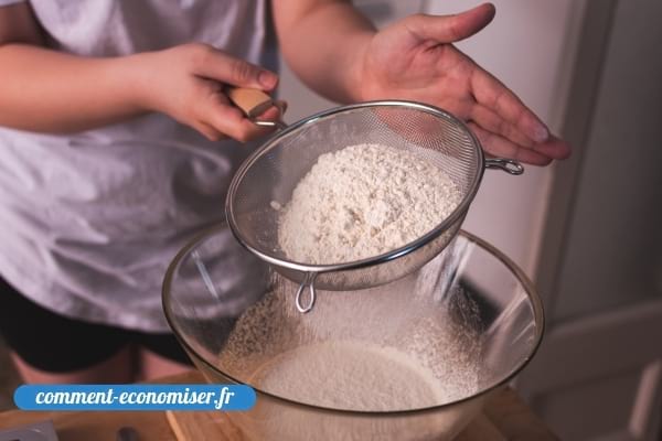 Une femme qui passe de la farine au tamis dans un saladier.