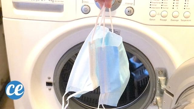 Des masques tenus à la main devant une machine à laver blanche ouverte