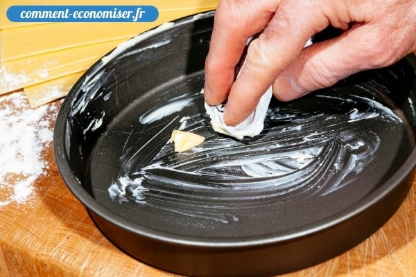 Une main qui étale du beurre à l’intérieur d'un moule à gâteau.