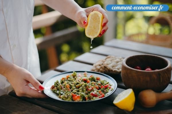 Une main qui ajoute un filet de jus de citron pressé dans un plat.