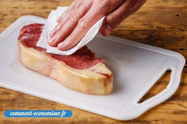 Une main qui sèche de la viande avec un essuie-tout.