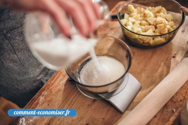 Une main qui pèse du sucre avec une balance de cuisine.