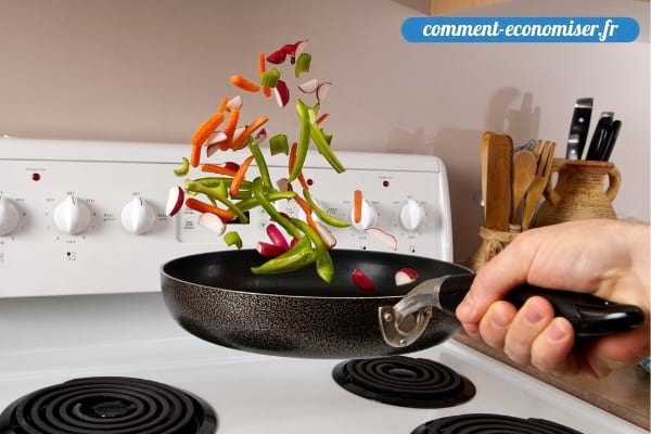 Une main qui fait sauter les légumes dans une poêle.