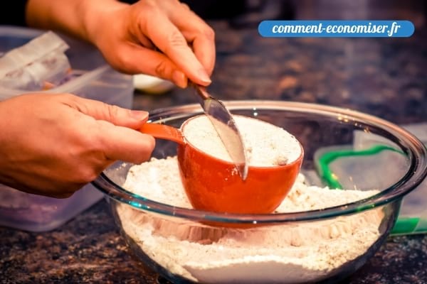 Une main qui nivèle la farine dans un tasse.