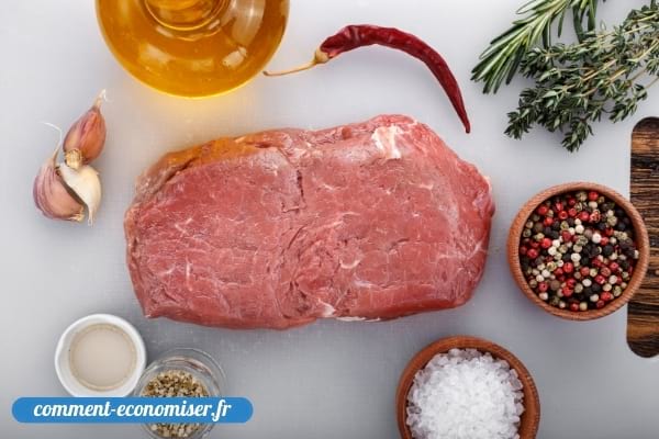 Une pièce de viande de bœuf crue et ses ingrédients pour l'assaisonner.