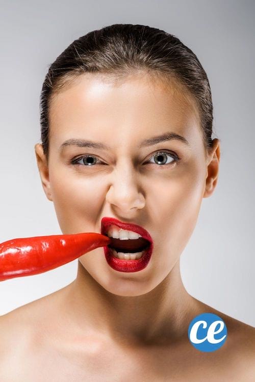 Une jeune femme brune avec des lèvres rouges croque un piment