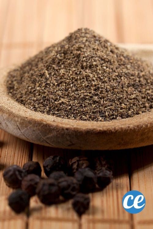 Du poivre moulu dans un plat sur une table en bois avec des grains de poivre noirs
