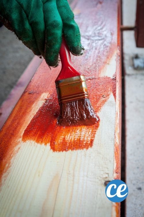 Une personne avec un gant vert peint une planche en bois en rouge