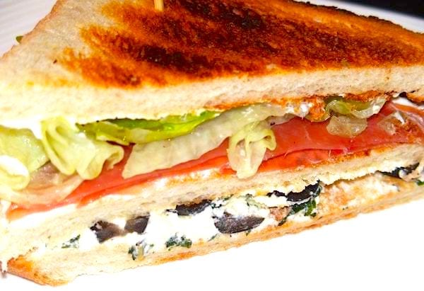 Sandwich au pain de mie avec du fromage de chèvre, des olives et du jambon cru et des légumes