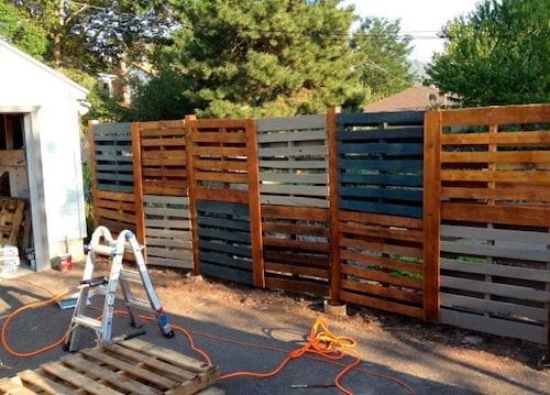 A high fence with a double height of wooden pallets.