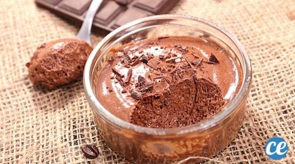 Une mousse au chocolat  dans un ramequin entamée avec une petite cuillère pleine de chocolat et une tablette sur de la toile de jute