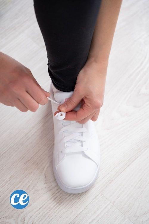 une personne noue les lacets d'une basket blanche
