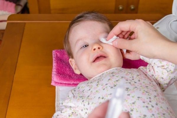 Une personne nettoie les yeux de bébé avec du sérum physiologique et une compresse