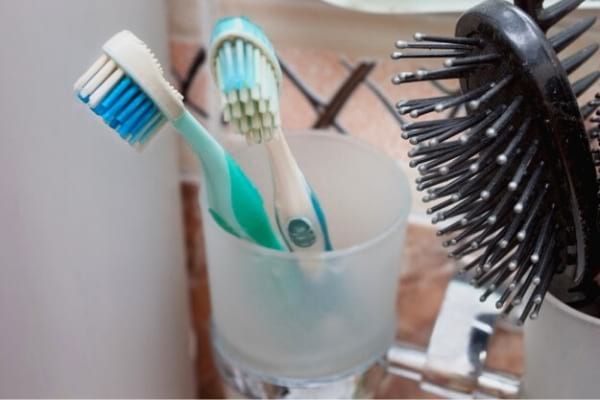 Deux brosses à dents dans un gobelet avec une brosse à cheveux dans une salle de bain 
