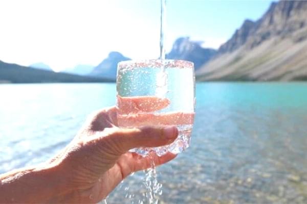 De l'eau du robinet qui coule dans un verre au bord d'un lac