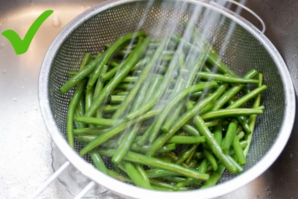Des haricots de conserve en train d'être lavés sous l'eau du robinet