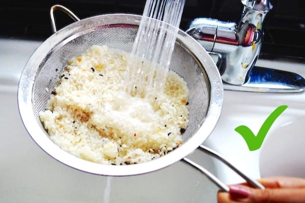 Du riz dans une passoire en train d'être lavé sous l'eau du robinet