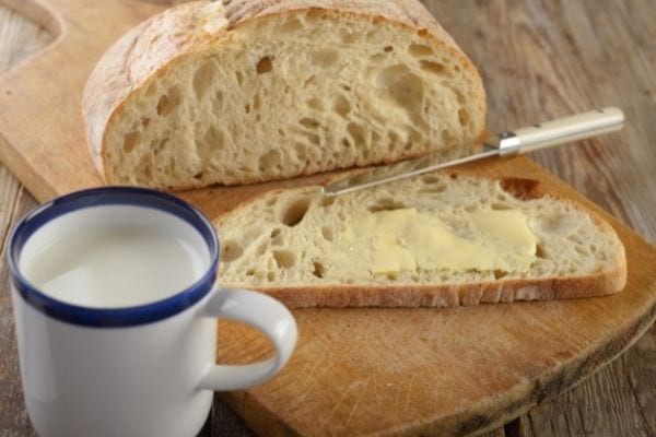 Une tartine de pain beurrée avec une tasse de lait et du pain sur une planche à découper