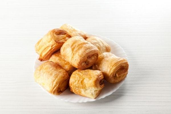 Plusieurs feuilletés à la saucisse qui ont été faits avec du jaune d'oeuf dans une assiette
