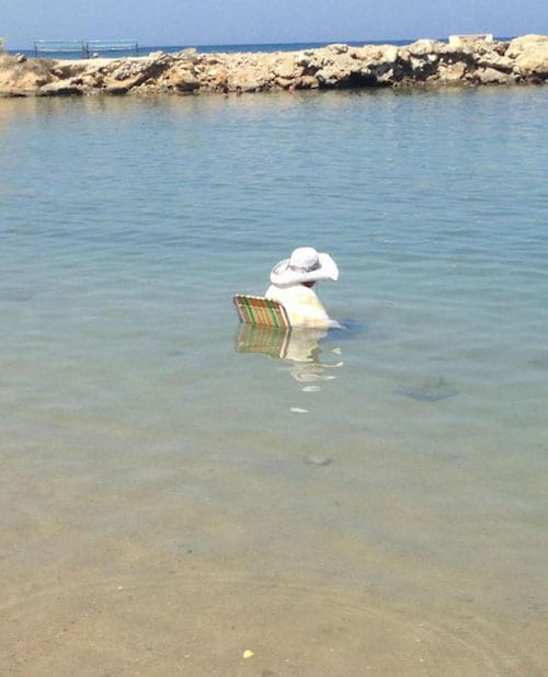 Une femme à chapeau assise sur une chaise au milieu de la marée 