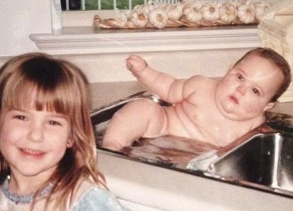 Petite fille souriante avec un bébé grassouillet dans un évier faisant un bain 