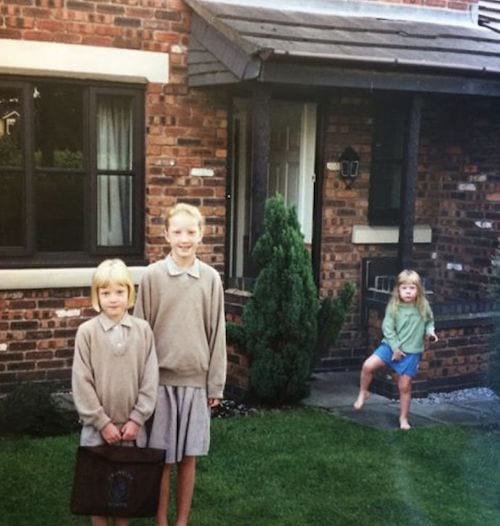 Deux jeunes filles en uniforme avec une autre petite fille derrière devant une maison 