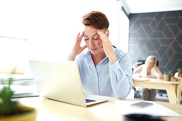 Une femme aux cheveux courts se tient les tempes devant son ordinateur portable