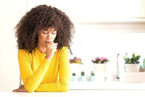 Une femme afro avec un pull jaune tousse le poing devant la bouche