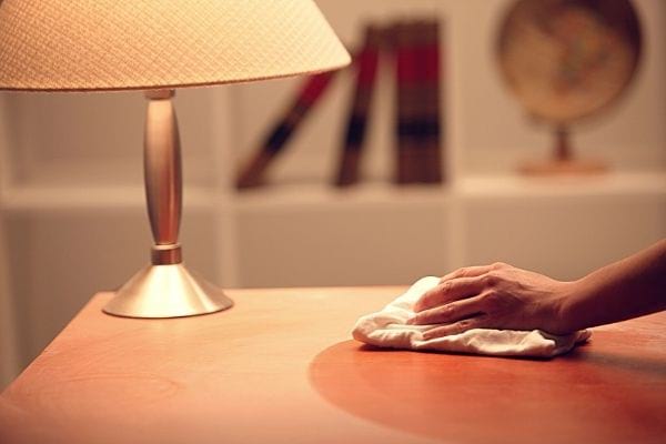 Une femme essuie la poussière sur une table avec une lampe pleine de poussière