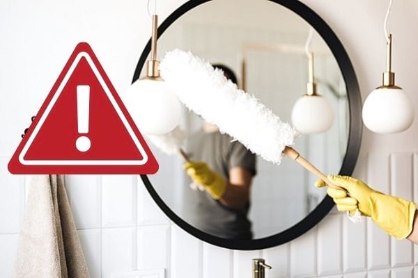 Une personne enlève la poussière sur des luminaires dans la salle de bain avec un plumeau