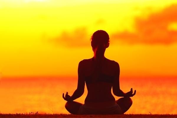 Une femme zen grâce aux bienfaits de la banane assise devant couché de soleil